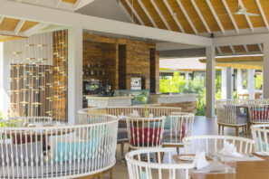 Moderní restaurace pod širým nebem s&nbsp;kulatými bílými židlemi, dřevěnými stoly, barevnými polštáři a&nbsp;pultem s&nbsp;kávovary. Prostor naplňuje přirozené světlo, které zvýrazňuje dřevěný strop a&nbsp;výhled do&nbsp;zahrady.