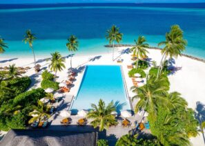 Sun Siyam Iru Veli na&nbsp;Maledivách. Letecký pohled na&nbsp;tropický plážový resort s&nbsp;velkým obdélníkovým bazénem, obklopený palmami, lehátky, bílým pískem a&nbsp;tyrkysovým oceánem pod jasně modrou oblohou.