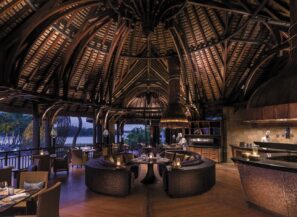 Elegantní tropická restaurace s&nbsp;vysokými dřevěnými stropy, útulným kulatým posezením a&nbsp;jemným ambientním osvětlením. Velká otevřená okna odhalují palmy a&nbsp;výhled na&nbsp;venkovní nábřeží a&nbsp;vytvářejí příjemnou a&nbsp;hřejivou atmosféru.