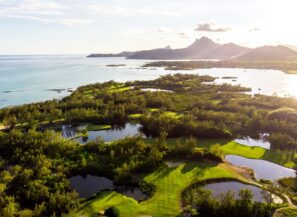 Letecký pohled na&nbsp;svěže zelené golfové hřiště s&nbsp;několika rybníky, obklopené hustými stromy v&nbsp;blízkosti pobřeží. Pod jasnou slunečnou oblohou je vidět oceán a&nbsp;vzdálené hory.