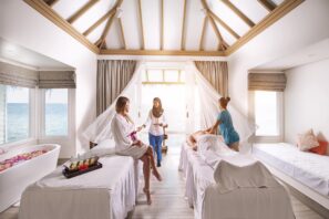 Ve světlé lázeňské místnosti s&nbsp;výhledem na&nbsp;oceán jsou dvě ženy v&nbsp;županech, jedna sedí a&nbsp;druhá leží na&nbsp;masážním stole, zatímco dva zaměstnanci poskytují procedury. Velkými okny sem proudí sluneční světlo a&nbsp;dodává prostoru uvolňující atmosféru.