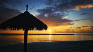 Na pozadí zářivého západu slunce nad klidným mořem, s&nbsp;mraky roztroušenými po&nbsp;obloze a&nbsp;sluncem odrážejícím se na&nbsp;vodě u&nbsp;obzoru, se rýsuje silueta slaměného slunečníku.