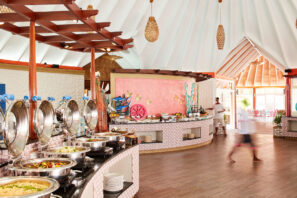 Světlá, vzdušná bufetová restaurace s&nbsp;talíři plnými jídla, barevnými nástěnnými obrazy, dřevěnými podlahami a&nbsp;slunečním světlem, které prochází kolem bufetového pultu.