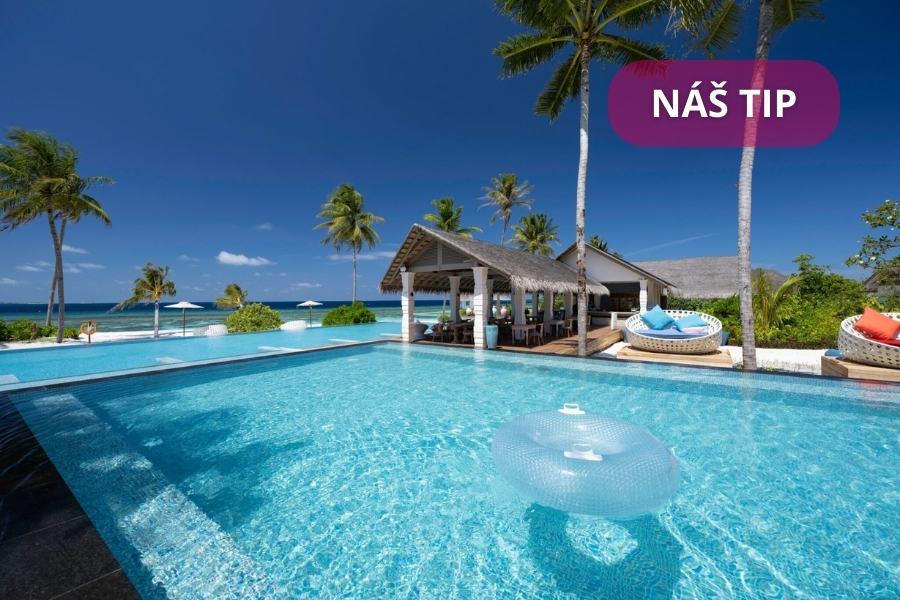 Tropický resort s&nbsp;velkým bazénem, palmami a&nbsp;lehátky u&nbsp;oceánu pod jasně modrou oblohou. V&nbsp;bazénu je průhledný nafukovací plovák. Na&nbsp;fialovém štítku je napsáno NÁŠ TIP.
