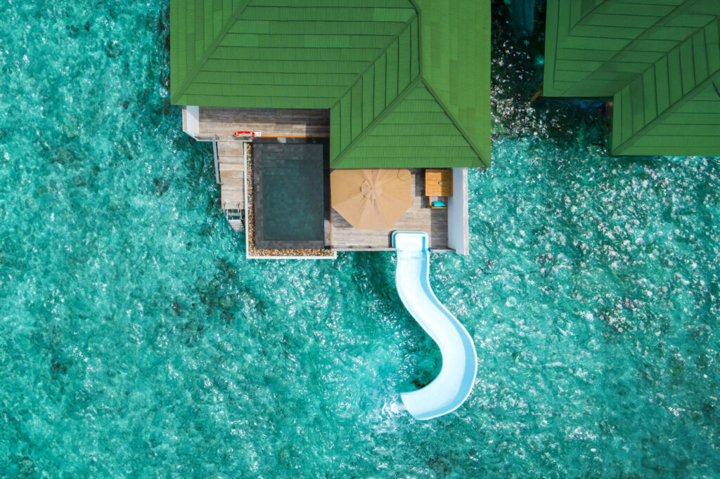 Panoramatický letecký snímek celého ostrova Siyam World obklopeného korálovými útesy s&nbsp;dlouhými moly s&nbsp;vodními vilami.