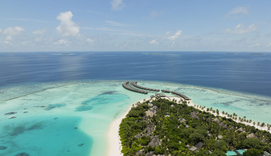 Letecký pohled na&nbsp;tropický ostrov Sun Siyam Iru Fushi obklopený rozlehlou tyrkysovou lagunou a&nbsp;korálovým útesem na&nbsp;Maledivách.